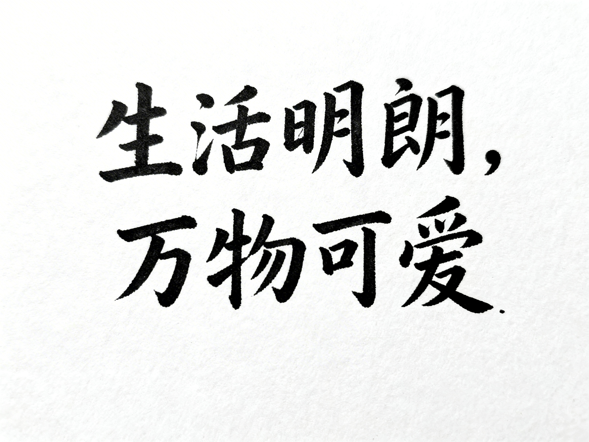 画面中是一张以纯白色为背景的简约书法图片，背景带有细微的纸张纹理感。图片中心位置分布着两行黑色的手写体中文书法，文字内容为“生活明朗，万物可爱”。第一行是“生活明朗”四个字，末尾带有一个逗号；第二行是“万物可爱”四个字，末尾有一个句号。字迹呈现出毛笔书写的质感，笔画粗细有致，风格清秀且有力。

作为一张 AI 生成的图片，画面中存在一些明显的文字结构缺陷：第一行的“活”字左侧三点水与右侧部分过于拥挤，且右侧的“舌”部结构略显扭曲；“朗”字的左侧“良”部笔画交代不清，显得有些破碎。第二行的“物”字左侧牛字旁与右侧部分连接处生硬，且“爱”字的下半部分笔画出现了不自然的粘连和变形。整体而言，虽然文字可辨认，但细节处缺乏真实书法的流畅度与结构严谨性。