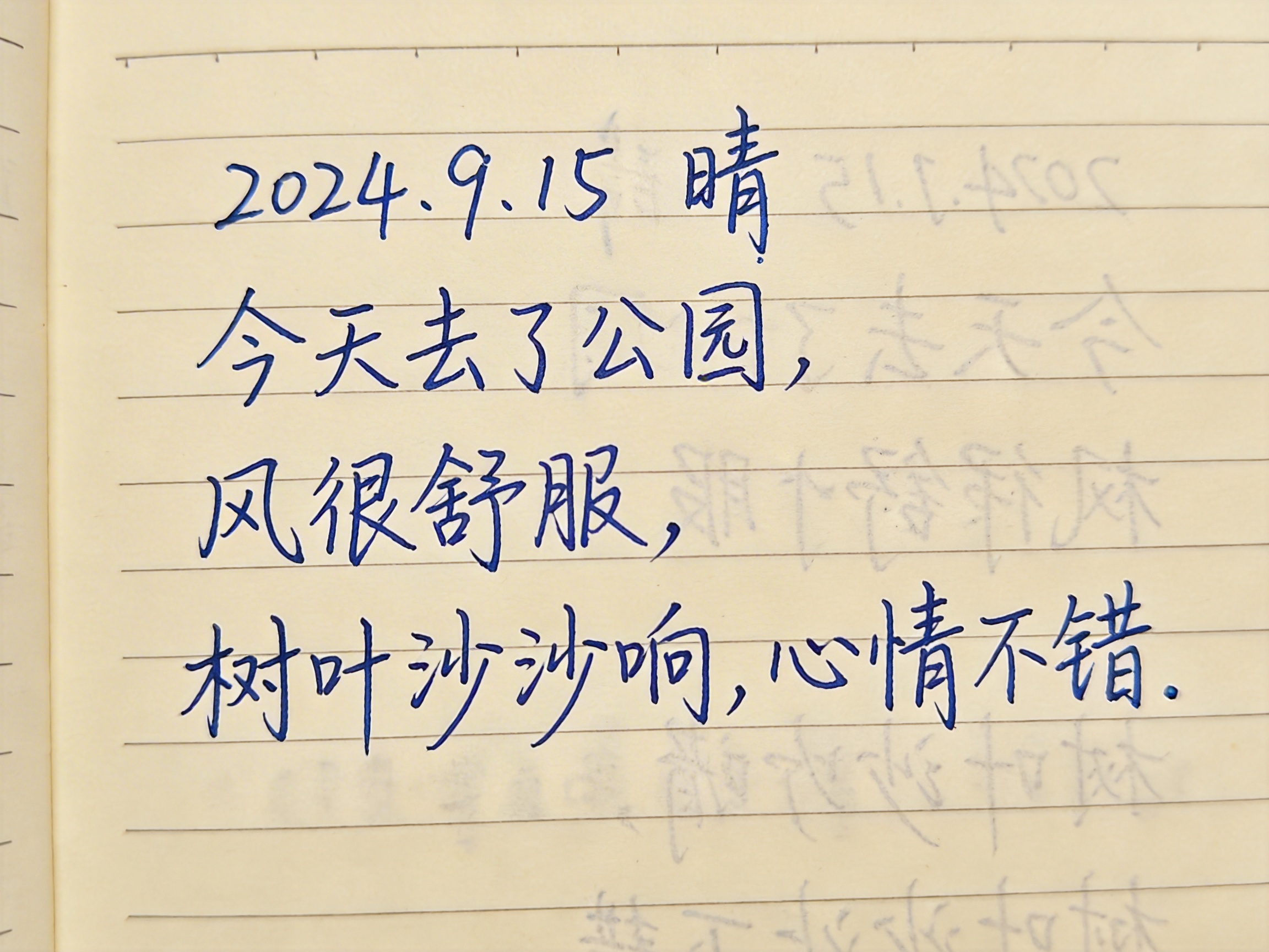 图中展示了一张模拟手写日记的近景照片。画面主体是一本米黄色横格纸笔记本，上面用蓝色圆珠笔书写了四行中文。文字内容为：“2024.9.15 晴，今天去了公园，风很舒服，树叶沙沙响，心情不错。”字迹工整且带有连笔，试图模仿真实的人类书写习惯。

然而，画面中存在明显的 AI 生成缺陷：在蓝色字迹的右侧，出现了大量杂乱、模糊且呈镜像对称的灰色虚影，这些虚影并非正常的透纸墨迹，而是逻辑混乱的笔画残留，甚至出现了反向的数字和汉字结构。此外，纸张左侧的装订线区域透视关系生硬，横格线的间距在边缘处略显不自然。整体光影均匀得近乎平面，缺乏真实纸张应有的微小起伏和纤维质感。