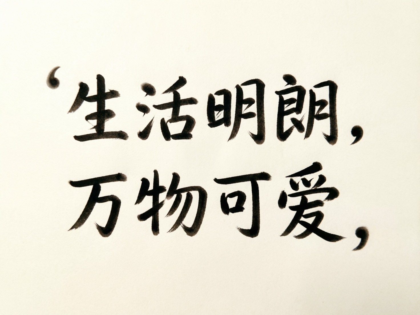 图中展示了一张以米白色为底色的书法作品，画面中心分布着两行黑色的手写体中文字符。第一行文字是“生活明朗”，第二行是“万物可爱”，文字风格介于行书与楷书之间，笔触带有明显的毛笔质感，墨色浓淡不一，展现出一种文艺且清新的视觉风格。在文字的左上角和右侧边缘，还点缀着类似逗号或引号的黑色墨点。

作为一张 AI 生成的图片，画面中存在明显的文字结构和逻辑缺陷。首先，第一行开头的符号位置尴尬，既不像标准的引号也不像装饰；其次，文字的笔画细节存在 AI 特有的扭曲，例如“活”字的左侧三点水连接生硬，“朗”字的月字旁内部横画模糊不清。最明显的错误在于标点符号的滥用，第一行末尾和第二行末尾都出现了形状怪异、位置随意的逗号，且第二行的“爱”字下方钩笔处显得支离破碎，缺乏真实书法的连贯气韵。