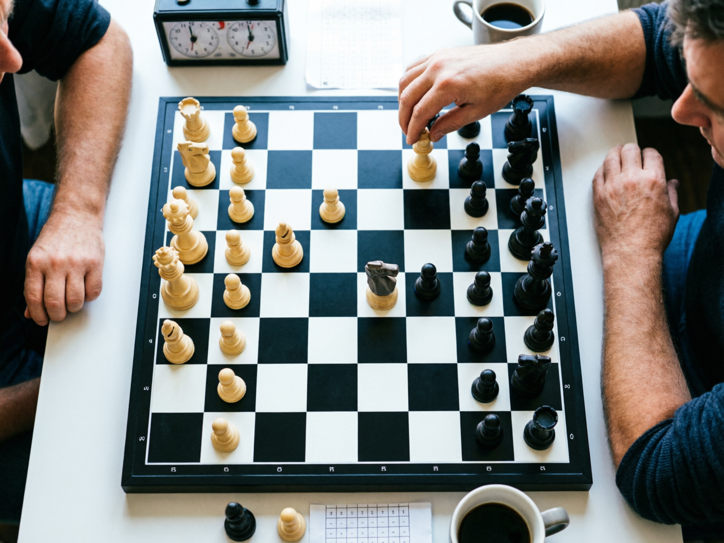 图中展示了一个从俯视角度拍摄的国际象棋对弈场景。画面中心是一块黑白相间的棋盘，两名中年男子分别坐在棋盘两侧，只能看到他们的手臂和部分侧脸。右侧的男子正伸手移动一枚白色棋子。桌面上除了棋盘，还摆放着一个复古的国际象棋计时钟、两杯黑咖啡和几张记谱纸。整体色调明亮，以白色桌面为背景，营造出一种专注的博弈氛围。

然而，画面中存在多处明显的 AI 生成缺陷。首先，棋盘的格数不正确，标准的国际象棋棋盘应为 8x8，但图中横向出现了 9 个格子，纵向格数也混乱不齐。其次，棋子的逻辑完全错误，棋盘上出现了过多的白色王后和主教，且棋子的底座与棋盘格子的位置关系扭曲。最明显的缺陷在于人物的手部：右侧男子的右手手指线条模糊且结构异常，左手则显得过于宽大。此外，计时钟上的刻度和指针杂乱无章，完全不符合物理逻辑。