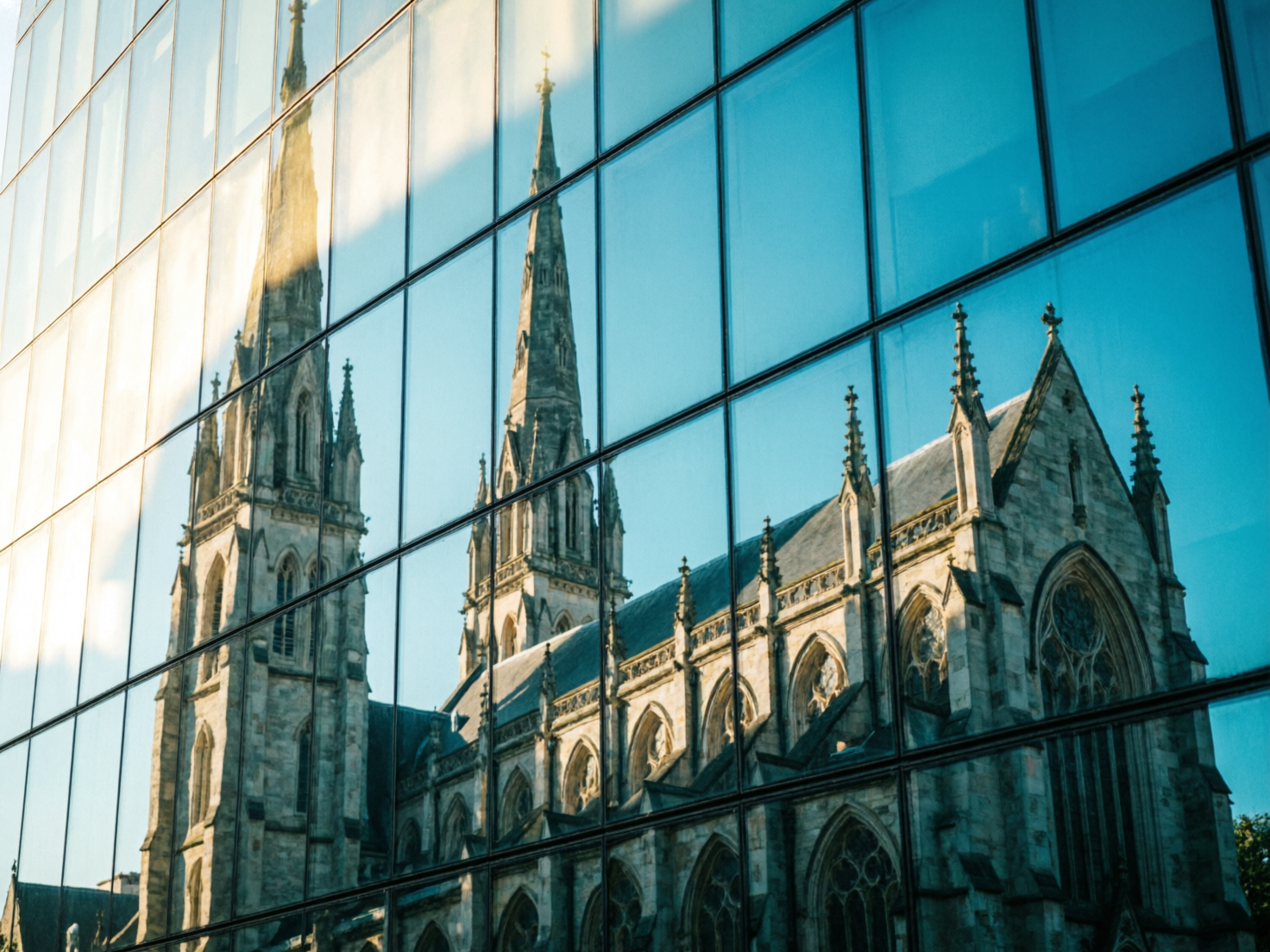 图中展示了一座宏伟的哥特式教堂倒映在现代办公大楼的玻璃幕墙上。画面构图巧妙，利用玻璃窗格的黑色框架将倒影分割成多个矩形块，形成了古典与现代交织的视觉冲击。教堂呈现出浅灰色的石质纹理，拥有高耸的尖塔、精美的尖拱窗和细长的扶壁，在午后温暖的阳光照射下，受光面泛着金色的光泽，与深蓝色的玻璃背景形成鲜明对比。

然而，画面中存在明显的 AI 生成缺陷。首先，教堂的结构在跨越不同玻璃窗格时出现了严重的透视错位和断裂，左侧尖塔的线条无法在相邻窗格间自然衔接。其次，建筑细节存在逻辑错误，例如教堂顶部的尖刺装饰分布杂乱且形状模糊，部分窗户的内部构造显得扭曲且不对称。此外，玻璃幕墙左侧的强光反射过于均匀，缺乏真实环境中光线散射的自然层次感。