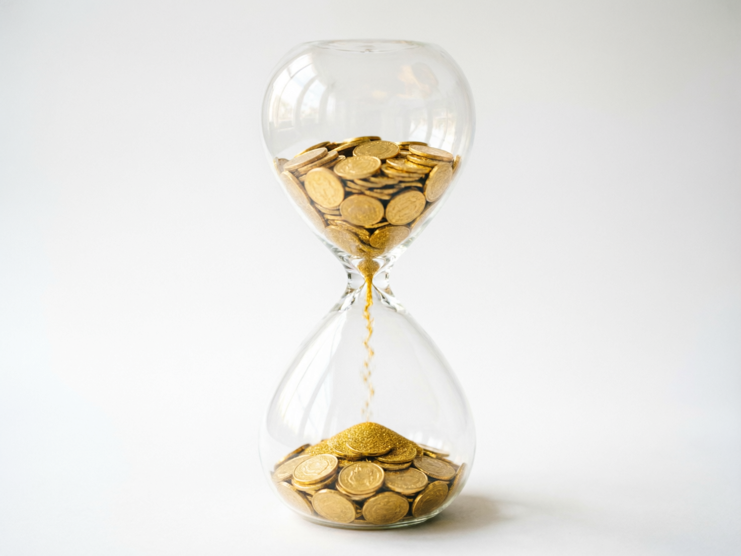图中展示了一个放置在纯白色背景中央的透明玻璃沙漏，寓意着“时间就是金钱”。沙漏的上半部分装满了金灿灿的硬币，而下半部分则堆积着一些硬币以及由上方落下的金色细砂。整体色调以简洁的白色和闪耀的金黄色为主，构图居中，光线明亮且柔和。

然而，画面中存在明显的 AI 生成缺陷：首先，物理逻辑存在矛盾，沙漏上部装的是大尺寸硬币，但通过中间狭窄颈部流下的却是细小的金砂，硬币并没有实际掉落的物理空间；其次，硬币的细节模糊，表面的浮雕图案杂乱无章，不符合任何真实货币的特征；最后，沙漏底部的硬币与金砂融合得不够自然，部分硬币的边缘显得生硬且透视关系略显扭曲。尽管如此，图片依然清晰地传达了关于财富与时间流逝的视觉概念。