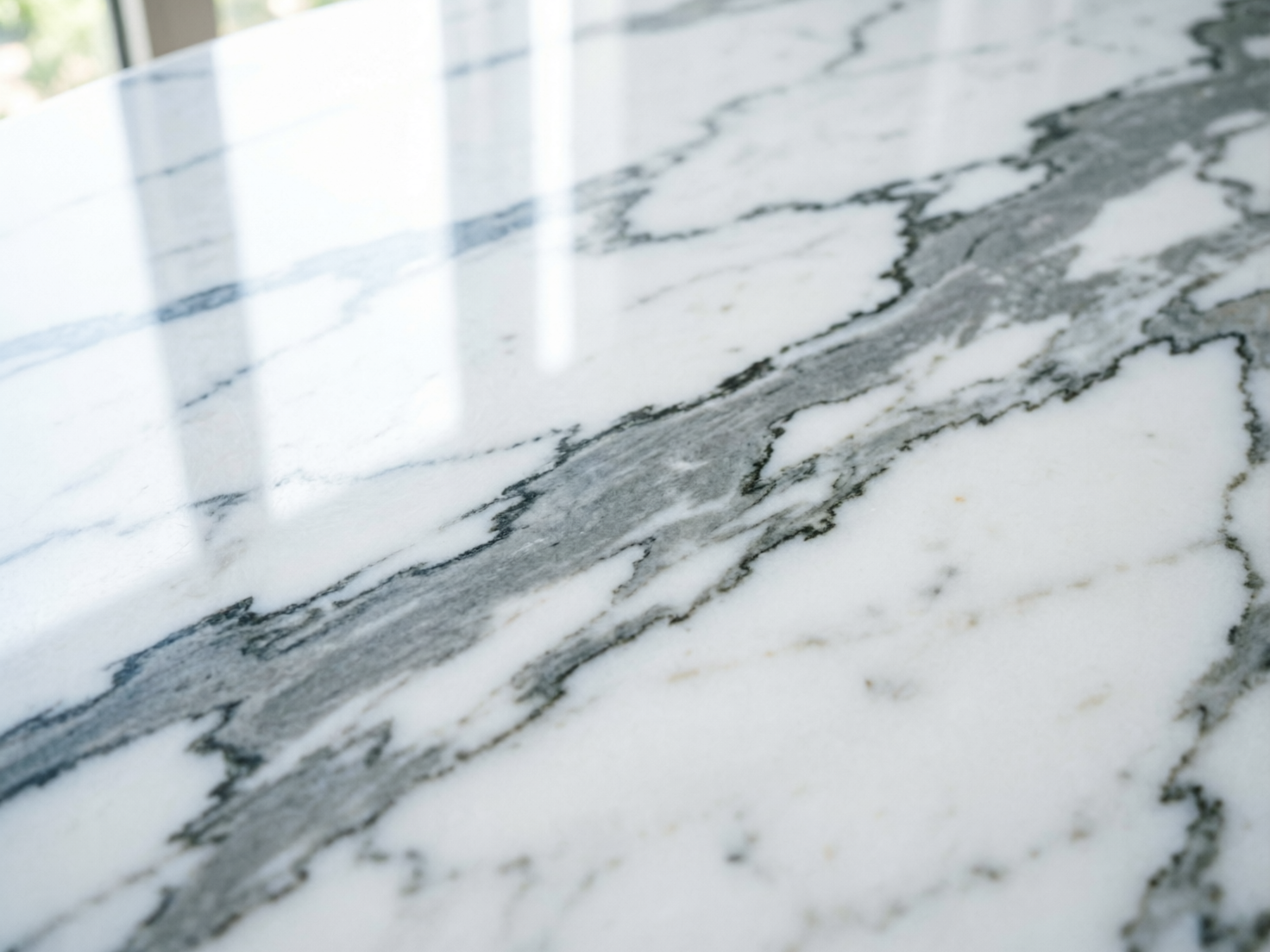 图中展示了一张近距离拍摄的大理石台面。画面以白色为基调，表面布满了深灰色和黑色的天然纹理，这些纹理如同水墨画般交错延伸，呈现出一种冷峻而优雅的质感。构图采用了斜向透视，焦点集中在画面中部的纹理细节上，而远处的背景则逐渐模糊。台面左上方有明显的反光，倒映出窗户的轮廓，显示出石材表面经过了精细的抛光处理，光泽感极强。作为一张 AI 生成的图片，其明显的缺陷在于左上角反光区域的透视逻辑不够严谨，倒映出的窗框线条显得有些扭曲且不连贯，与真实的物理反射规律略有出入。此外，部分细微纹理在边缘处显得过于锐利，缺乏天然石材那种自然的过渡感。总体而言，画面营造出了一种现代、简约的室内装饰氛围。