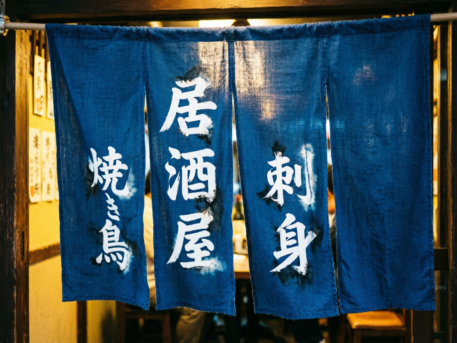 图中展示了一家充满怀旧氛围的日式居酒屋入口。画面主体是一幅深蓝色的布帘（暖帘），悬挂在木质门框上，布帘被分为四个长条部分。布帘上用白色书法字体写着「居酒屋」、「刺身」和「烧き鸟」等汉字。透过布帘的缝隙，可以看到店内昏黄温暖的灯光，以及模糊的食客身影和木质桌椅，营造出一种深夜食堂的温馨感。背景左侧墙上贴着一些白底黑字的菜单条。

在 AI 生成缺陷方面，画面存在明显的文字逻辑和笔画错误。最左侧布帘上的「烧き鸟」字样中，「烧」字的火字旁与右侧结构重叠混乱，「鸟」字的下半部分笔画扭曲且不完整。中间布帘的「居酒屋」中，「酒」字的氵部首与右侧部分连接异常。此外，左侧墙上的菜单文字完全是杂乱无章的线条，无法辨认。布帘上文字周围的白色晕染效果分布不自然，带有明显的数字模拟痕迹。