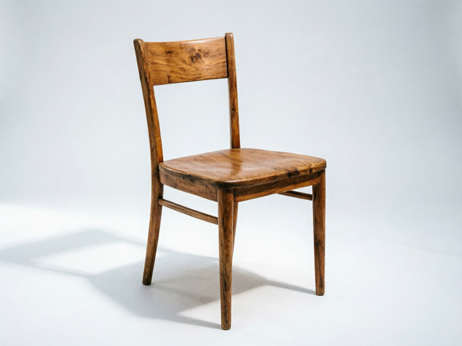 图中展示了一把孤立在纯净浅灰色背景下的木质餐椅。这把椅子呈现出深棕色的原木质感，表面带有明显的木纹、节疤和复古的磨损痕迹，整体风格简约且略显厚重。光线从左前方照射，在椅子右侧和后方的地面上投射出清晰的阴影。构图上，椅子略微向右侧偏转，展现出靠背、座面和四条椅腿的结构。

然而，画面中存在明显的 AI 生成缺陷：最显著的问题在于椅腿的数量和布局逻辑异常。虽然乍看有四条腿，但左侧前后的两条椅腿在底部几乎重合，且连接它们的横撑木位置不对称，导致结构在透视上显得混乱。此外，右侧椅腿与座面的连接处缺乏合理的物理衔接感，显得有些漂浮。座面的边缘线条也略显不平整，这些细节揭示了该图像并非真实摄影作品。