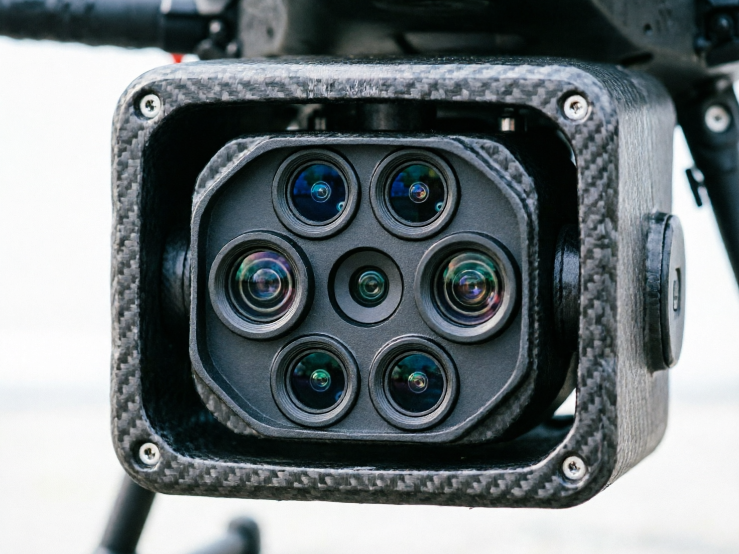 图中展示了一个安装在无人机底部的多镜头摄像系统。画面中心是一个方形的碳纤维外壳，表面呈现出清晰的灰色编织纹理，四个角各有一颗银色螺丝固定。外壳内部嵌套着一个黑色的镜头组，共有七个圆形镜头，排列方式类似蜂巢：中心一个微型镜头，周围环绕着六个较大的镜头。镜头玻璃反射出深蓝色、绿色和淡紫色的光泽，显得精密且具有科技感。背景是模糊的浅灰色，隐约可见无人机的黑色支架。

画面中存在明显的 AI 生成缺陷：首先，镜头组的排列并不完全对称，右侧的两个镜头边缘出现了不自然的融合与重叠；其次，最外层碳纤维外壳的边缘纹理在顶部和左侧显得模糊且断裂，缺乏真实的物理结构逻辑；此外，左上角的螺丝形状略显扭曲，与整体金属质感不符。这些细节揭示了图像是由算法合成而非真实拍摄。