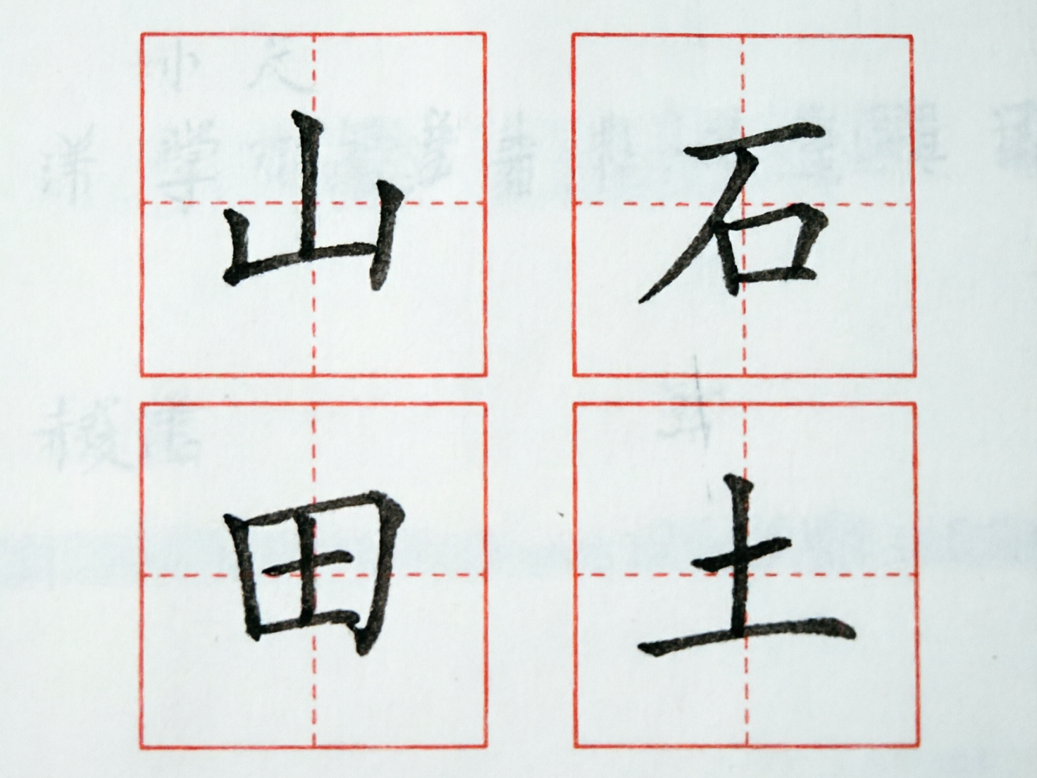 画面中展示了四个排列成两行两列的红色田字格，每个格子内都有一个黑色毛笔书写的汉字，背景是带有浅灰色模糊字迹的白色纸张。左上角是“山”字，右上角是“石”字，左下角是“田”字，右下角是“土”字。字体呈现出楷书风格，笔触带有水墨的质感。

这张图片存在明显的 AI 生成缺陷：首先，文字的结构和笔画逻辑不严谨，例如“山”字的左侧竖画与底横连接处断开，“田”字的内部横竖交汇处模糊且外框扭曲，“土”字的最后一横呈现出不自然的波浪状。其次，红色田字格的虚线定位不准，未能与汉字的结构中心对齐。最后，背景中隐约可见的浅色文字是一些无法辨认的乱码字符，且纸张边缘的红色边框线条粗细不均，显示出明显的算法合成痕迹。