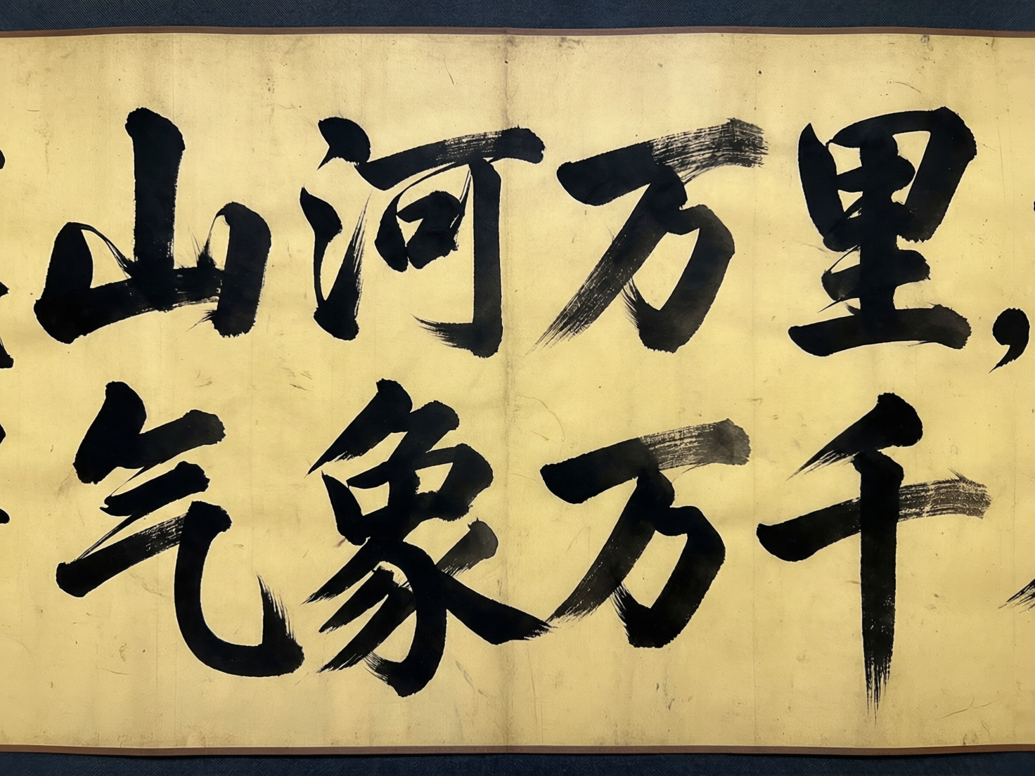 图中展示了一幅模拟中国传统书法横幅的 AI 生成图像。画面背景为带有陈旧质感的淡黄色宣纸，纸张中心有一条垂直的折痕。纸面上用浓重的黑色墨迹书写着两行汉字，字体风格介于行书与草书之间，笔触带有明显的枯笔飞白效果。第一行从左至右隐约可见“山河万里”四个字，第二行则是“气象万千”。然而，作为 AI 生成的作品，画面存在明显的逻辑与文字缺陷：文字的排版顺序混乱，不符合传统书法从右向左或现代从左向右的严谨规范；部分汉字的结构严重变形，例如“万”字的笔画显得生硬且不连贯，“千”字的末笔过长且缺乏力度变化。此外，背景纸张边缘的阴影处理不够自然，文字与纸张的融合度在细节处显得有些漂浮，缺乏真实墨汁渗入纸张纤维的质感。