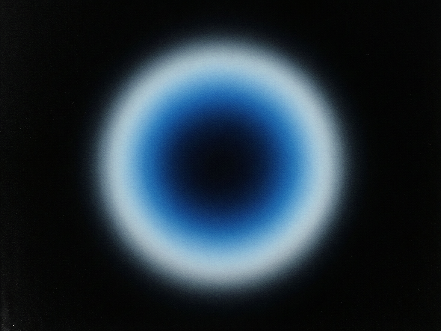 图中展示了一个位于纯黑色背景中央的圆形发光体，呈现出一种极简主义的抽象风格。这个圆形物体由内而外展现出层次分明的色彩梯度：最核心是一个深邃的黑色圆心，向外逐渐过渡为浓郁的深蓝色，再变为明亮的浅蓝色，最外圈则是一层柔和的白色光晕。整个圆形边缘具有明显的羽化效果，看起来像是一个模糊的焦点或一种弥散的光影，给人一种宁静、深邃且带有科技感的视觉体验。画面构图高度对称，色彩过渡平滑，具有细腻的颗粒感。作为一张 AI 生成的抽象图，其结构非常简单，没有复杂的人造元素或生物特征，因此不存在明显的肢体变形或逻辑错误，但可以观察到光晕的最外层边缘在纯黑背景下略显生硬，缺乏自然光线物理散射的随机性。