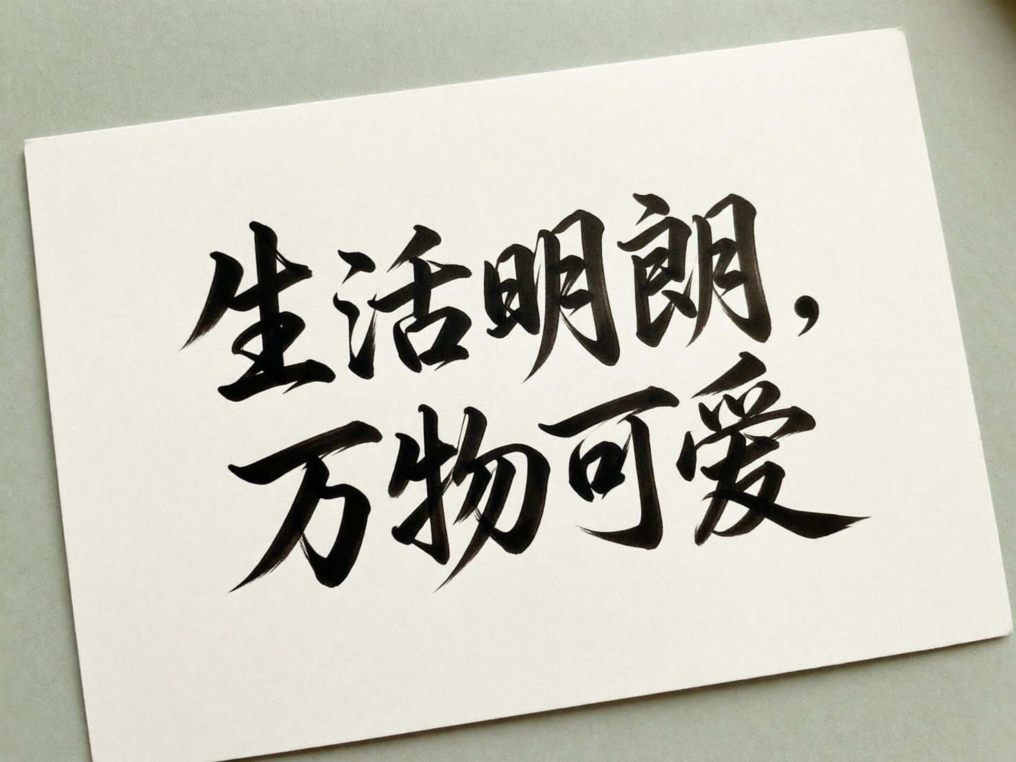 图中展示了一张斜放在淡绿色背景上的白色长方形卡片，卡片上书写着两行黑色的毛笔书法字体。文字内容本应为“生活明朗，万物可爱”，整体风格简约清新，墨色浓郁，笔触带有明显的干枯飞白效果。然而，作为一张 AI 生成的图片，画面中存在显著的文字结构错误：第一行的“活”字左侧偏旁与右侧部分重叠且结构扭曲，“明”字和“朗”字的笔画也出现了不自然的粘连与变形，失去了汉字的严谨间架结构。第二行的“万”字起笔处过于生硬，“物”字右侧的“勿”部笔画交错混乱，“爱”字的下半部分结构也显得模糊且不合常理。此外，卡片边缘与背景的透视关系略显生硬，缺乏真实的阴影过渡。
